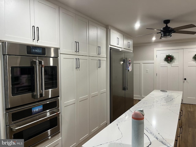 kitchen featuring light stone countertops, ceiling fan, dark wood-type flooring, stainless steel appliances, and white cabinets