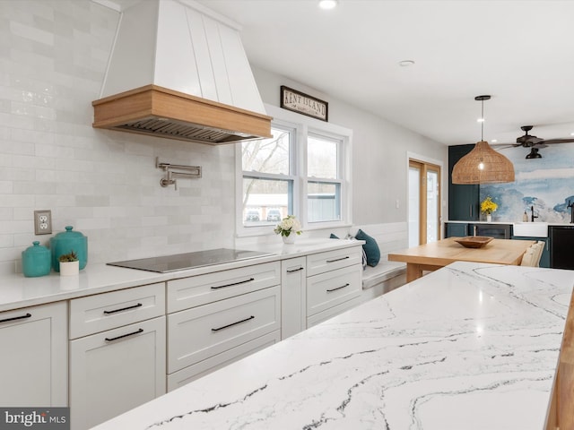 kitchen featuring pendant lighting, premium range hood, white cabinets, decorative backsplash, and black electric cooktop