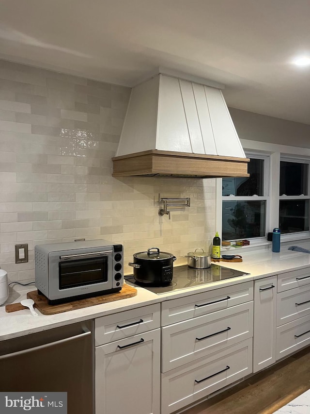 kitchen with white cabinets, stovetop, custom range hood, and backsplash