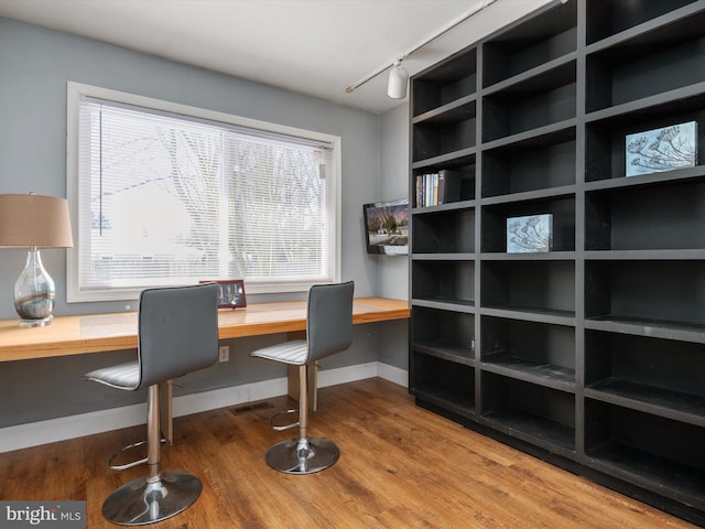 office space with built in desk, track lighting, and wood-type flooring