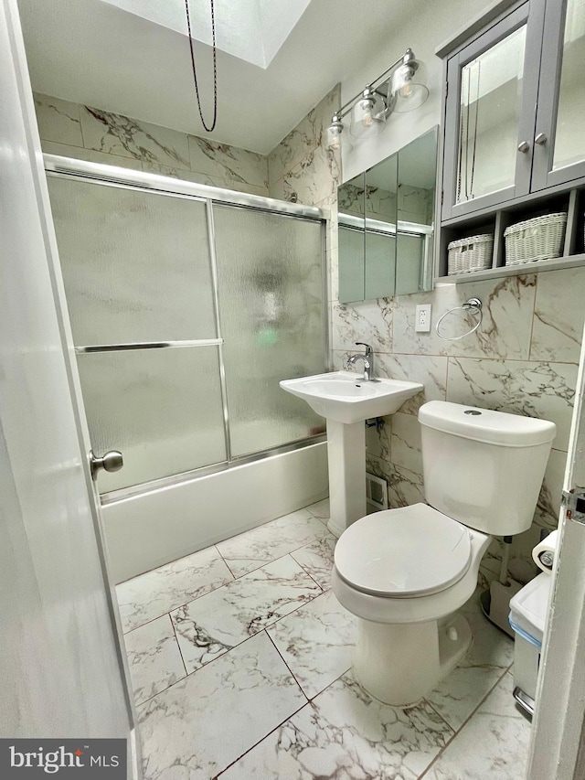 bathroom with toilet, combined bath / shower with glass door, and tile walls