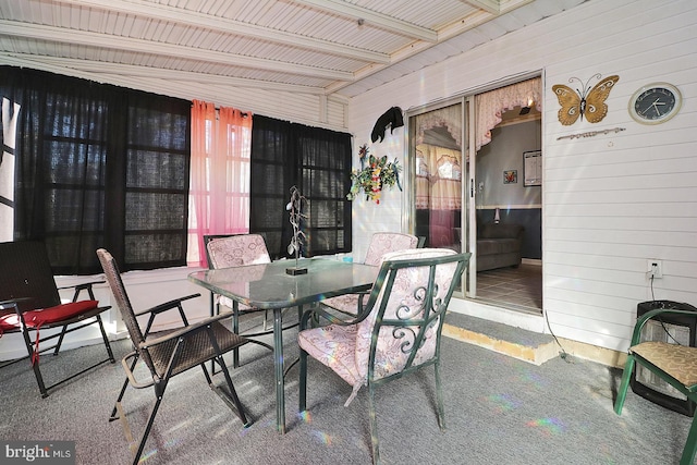 carpeted dining space with beamed ceiling and wooden walls