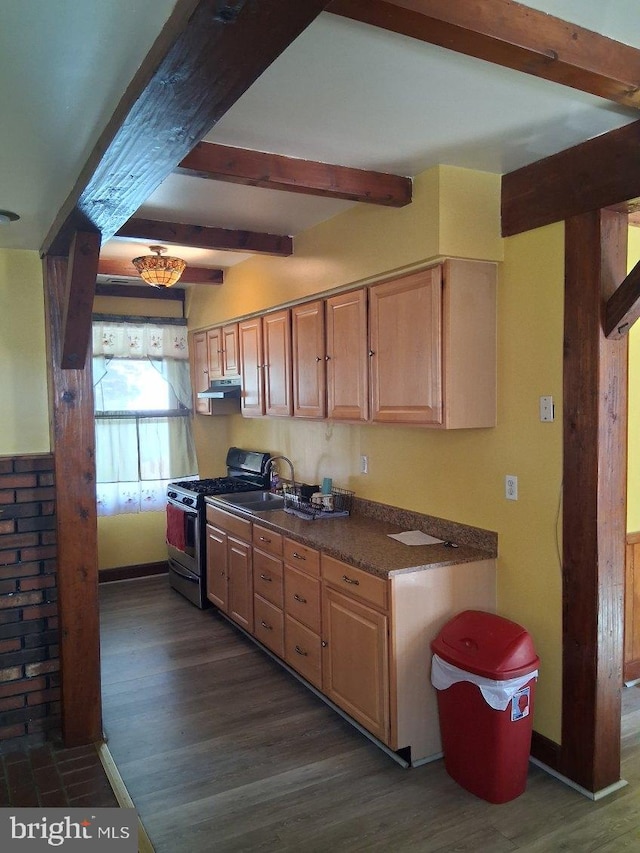 kitchen featuring beam ceiling, under cabinet range hood, dark wood-type flooring, dark countertops, and stainless steel gas range oven