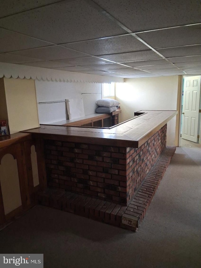 bar with a bar, carpet flooring, and a paneled ceiling