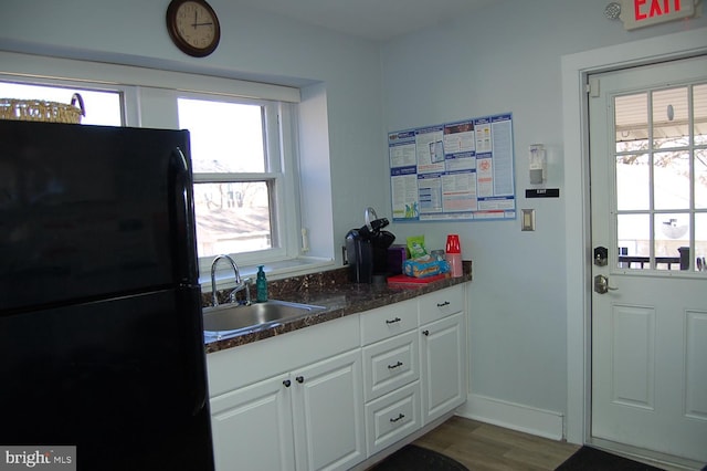 kitchen with black refrigerator, sink, dark stone countertops, white cabinets, and hardwood / wood-style floors