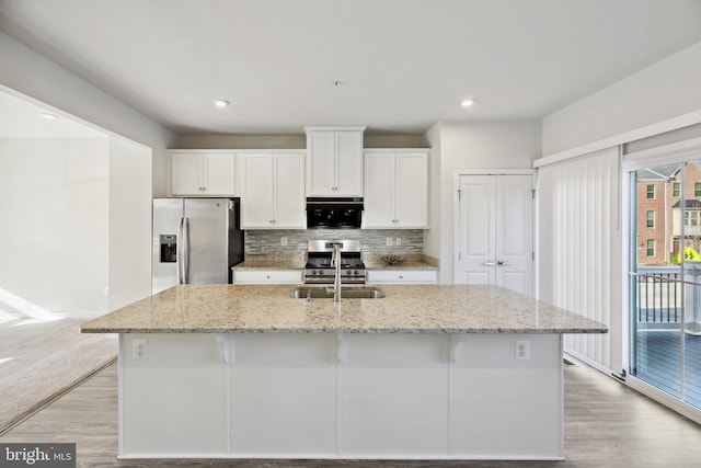 kitchen with light stone countertops, white cabinets, a center island with sink, and stainless steel appliances