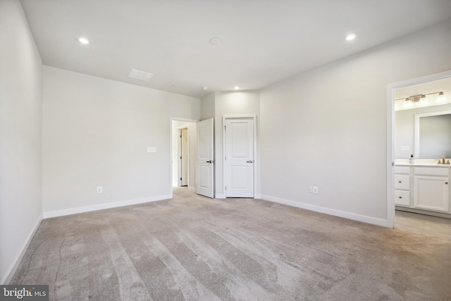 unfurnished bedroom featuring ensuite bath, light carpet, and sink