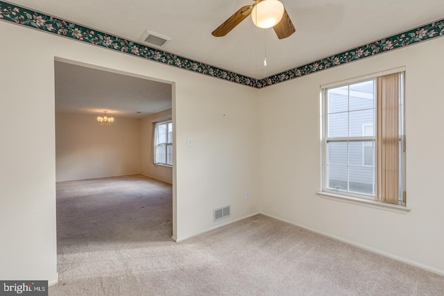 carpeted empty room with ceiling fan with notable chandelier and plenty of natural light