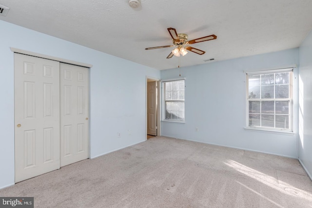 unfurnished bedroom with multiple windows, a closet, light colored carpet, and ceiling fan