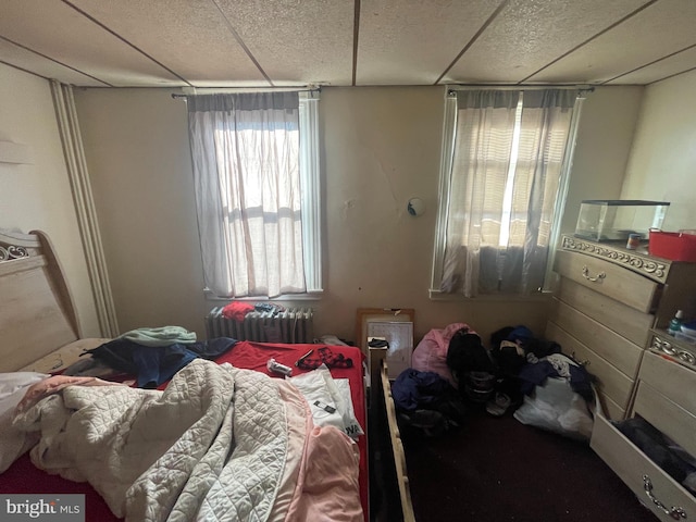 bedroom with a paneled ceiling and radiator heating unit