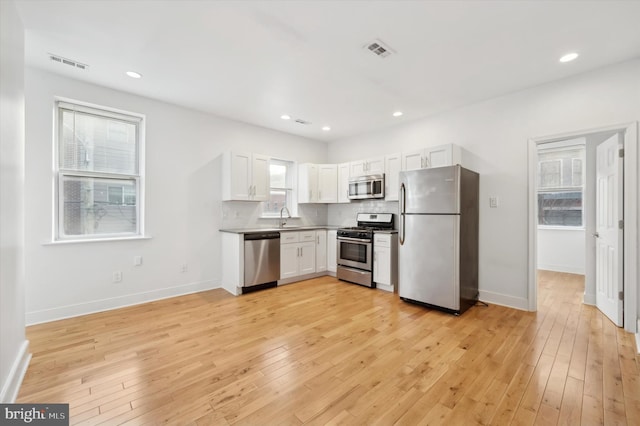 kitchen with decorative backsplash, stainless steel appliances, sink, light hardwood / wood-style flooring, and white cabinets