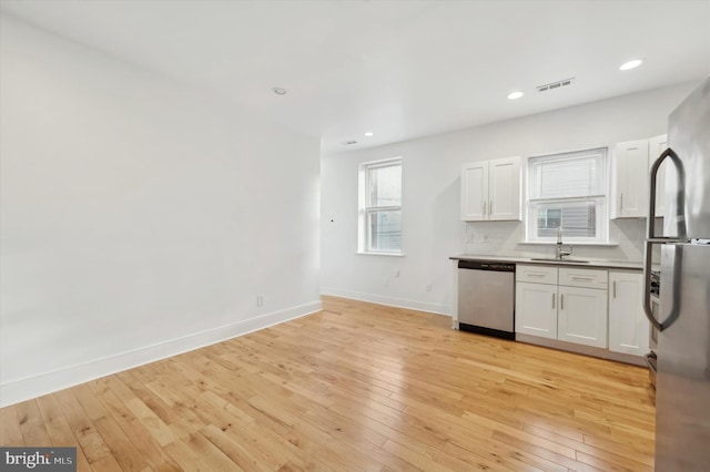 kitchen featuring backsplash, white cabinets, sink, light hardwood / wood-style flooring, and stainless steel appliances