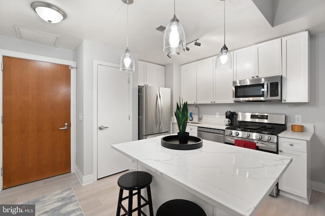 kitchen featuring white cabinetry, a center island, hanging light fixtures, stainless steel appliances, and light stone countertops