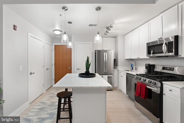 kitchen featuring sink, appliances with stainless steel finishes, hanging light fixtures, white cabinets, and a kitchen island