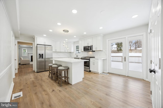 kitchen with white cabinetry, decorative light fixtures, decorative backsplash, a kitchen island, and appliances with stainless steel finishes