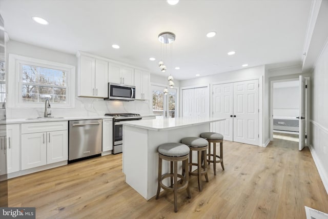 kitchen featuring stainless steel appliances, sink, white cabinets, a center island, and hanging light fixtures