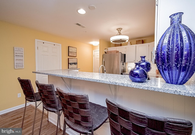 kitchen featuring a kitchen breakfast bar, stainless steel fridge, light stone countertops, and white cabinetry