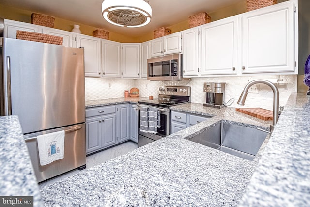 kitchen featuring appliances with stainless steel finishes, tasteful backsplash, light stone counters, sink, and white cabinetry