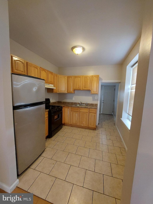 kitchen featuring black range with gas cooktop, sink, light brown cabinets, stainless steel refrigerator, and light tile patterned flooring