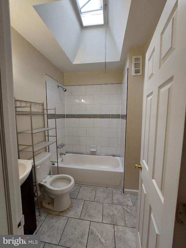 full bathroom with a skylight, vanity, tiled shower / bath, and toilet