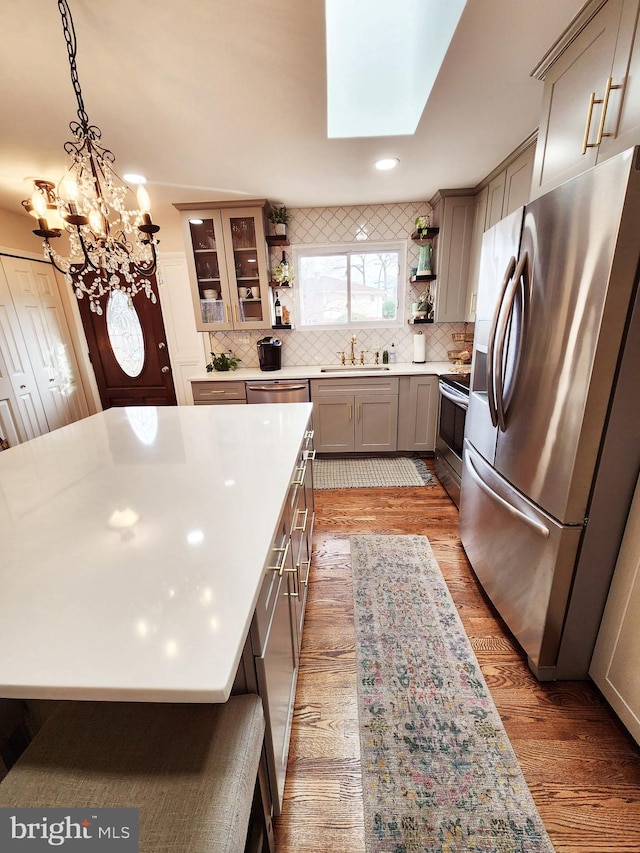 kitchen with stainless steel appliances, a skylight, sink, decorative light fixtures, and backsplash