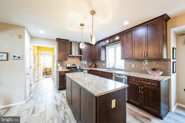 kitchen featuring pendant lighting, wall chimney range hood, sink, stainless steel appliances, and a kitchen island