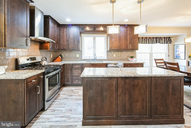 kitchen with wall chimney exhaust hood, sink, appliances with stainless steel finishes, pendant lighting, and light stone countertops