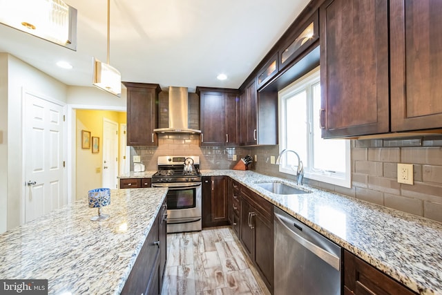 kitchen with pendant lighting, wall chimney range hood, sink, appliances with stainless steel finishes, and light stone countertops