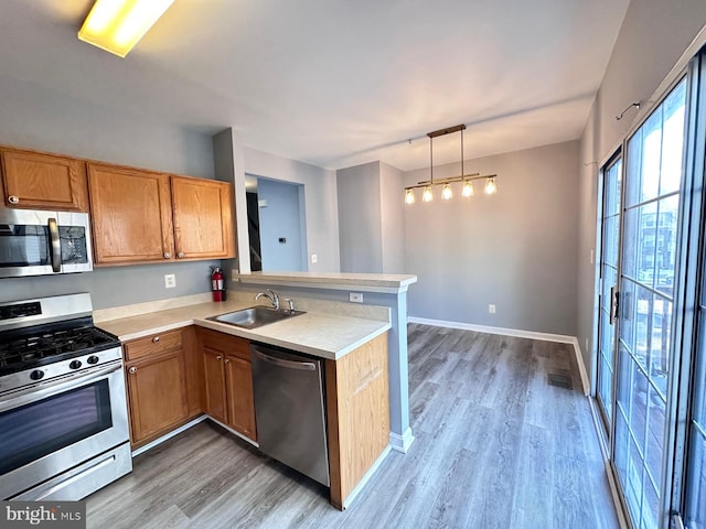 kitchen with sink, hanging light fixtures, kitchen peninsula, light hardwood / wood-style floors, and appliances with stainless steel finishes