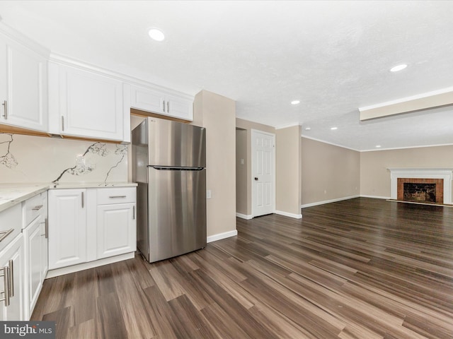 kitchen with stainless steel refrigerator, light stone countertops, a fireplace, and white cabinets