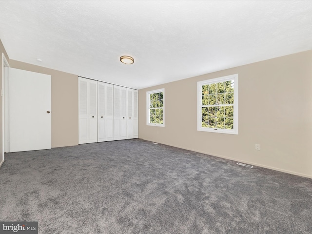 unfurnished bedroom featuring dark colored carpet and a textured ceiling