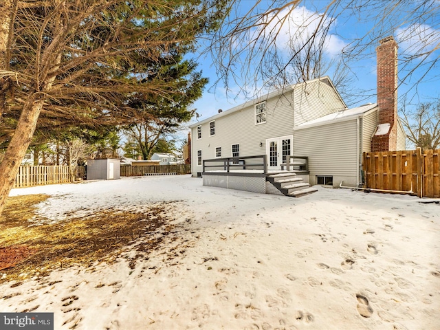 snow covered rear of property featuring a wooden deck, french doors, and a storage shed