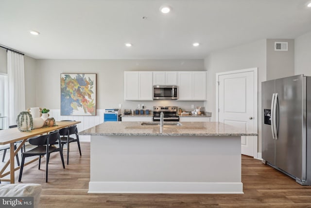 kitchen with light stone countertops, appliances with stainless steel finishes, white cabinetry, and an island with sink