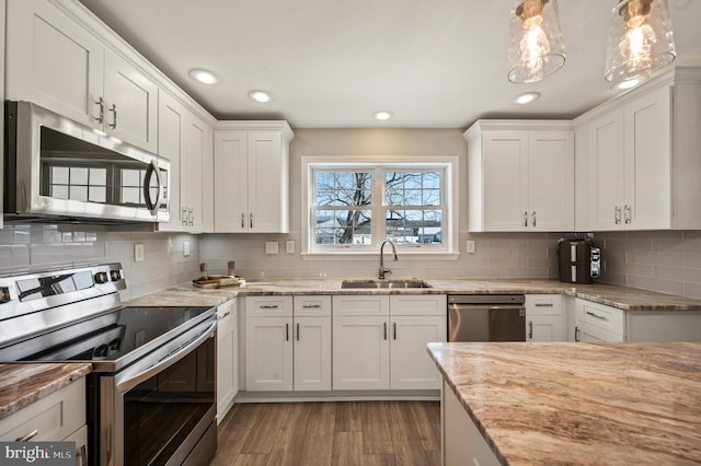 kitchen featuring appliances with stainless steel finishes, white cabinets, decorative light fixtures, and sink