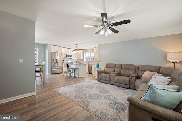 living room featuring ceiling fan with notable chandelier, light hardwood / wood-style floors, and sink