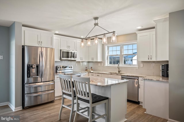 kitchen with light stone countertops, appliances with stainless steel finishes, a center island, white cabinetry, and hanging light fixtures