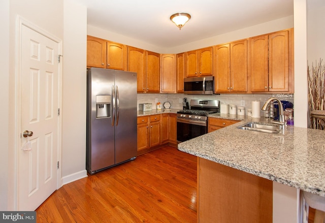 kitchen with appliances with stainless steel finishes, dark wood-type flooring, light stone counters, decorative backsplash, and sink