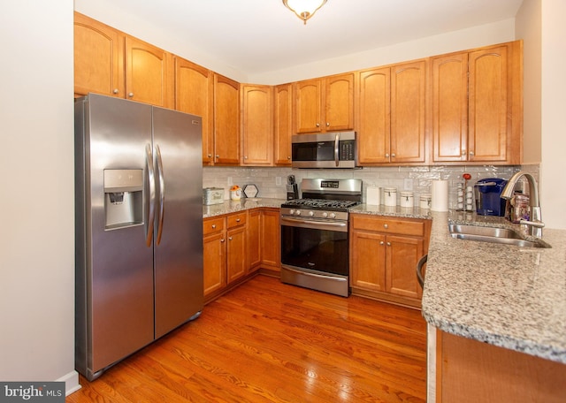 kitchen with light stone counters, hardwood / wood-style flooring, stainless steel appliances, tasteful backsplash, and sink