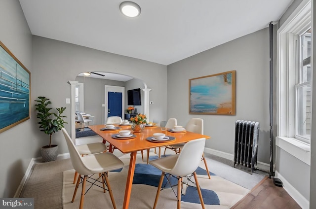 dining room featuring arched walkways, radiator heating unit, and baseboards