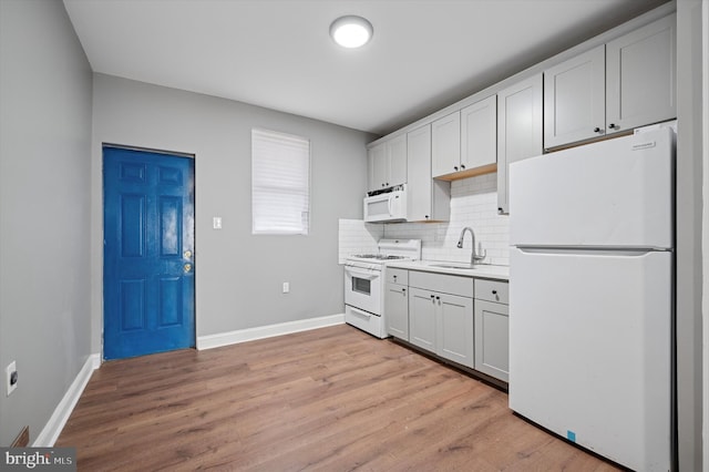 kitchen featuring light wood-style flooring, backsplash, a sink, white appliances, and baseboards