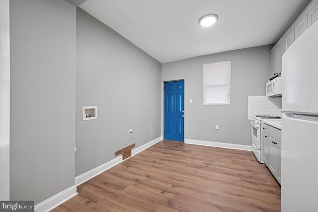 kitchen featuring white appliances, white cabinetry, baseboards, backsplash, and light wood finished floors