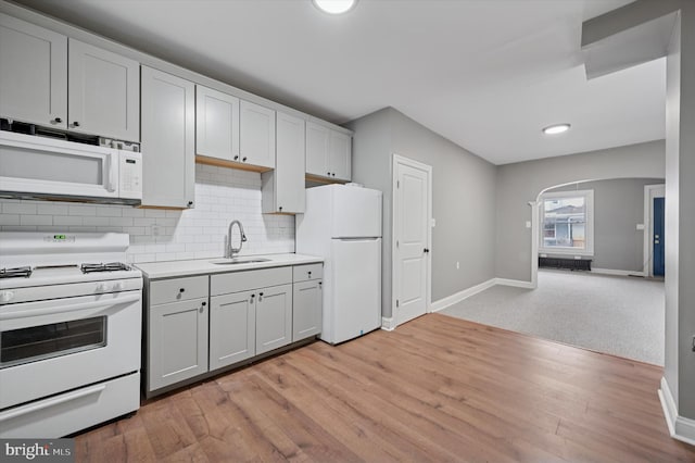 kitchen featuring light wood finished floors, light countertops, backsplash, a sink, and white appliances