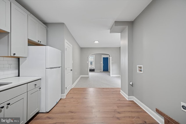 kitchen featuring baseboards, arched walkways, backsplash, and freestanding refrigerator