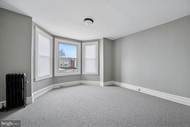 carpeted spare room featuring baseboards and radiator