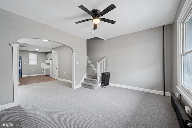 unfurnished living room featuring decorative columns, baseboards, arched walkways, carpet, and stairs