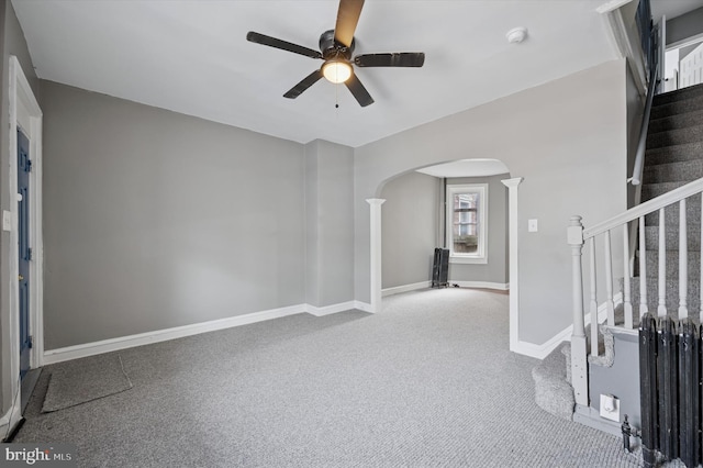 unfurnished room with arched walkways, carpet, ceiling fan, baseboards, and stairs