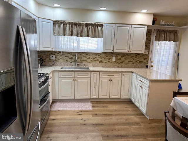 kitchen featuring a healthy amount of sunlight, light wood finished floors, a peninsula, a sink, and appliances with stainless steel finishes