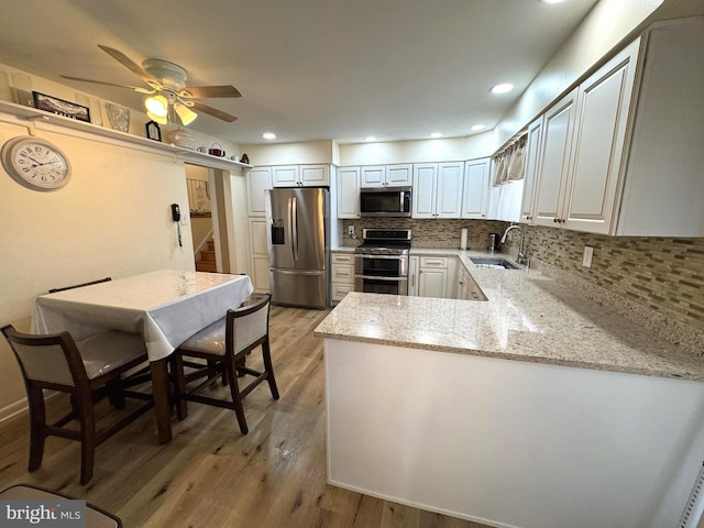 kitchen with light wood-type flooring, a sink, backsplash, appliances with stainless steel finishes, and light stone countertops