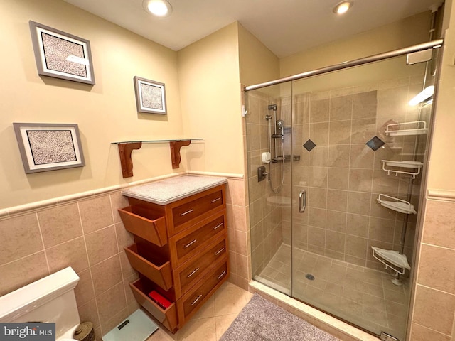 bathroom featuring a shower stall, toilet, wainscoting, tile patterned floors, and tile walls