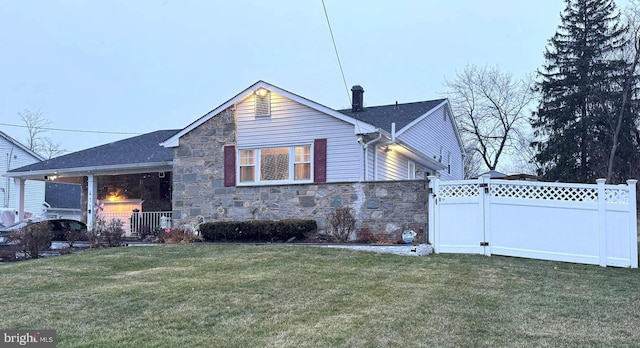 view of front facade featuring stone siding, a front yard, and fence